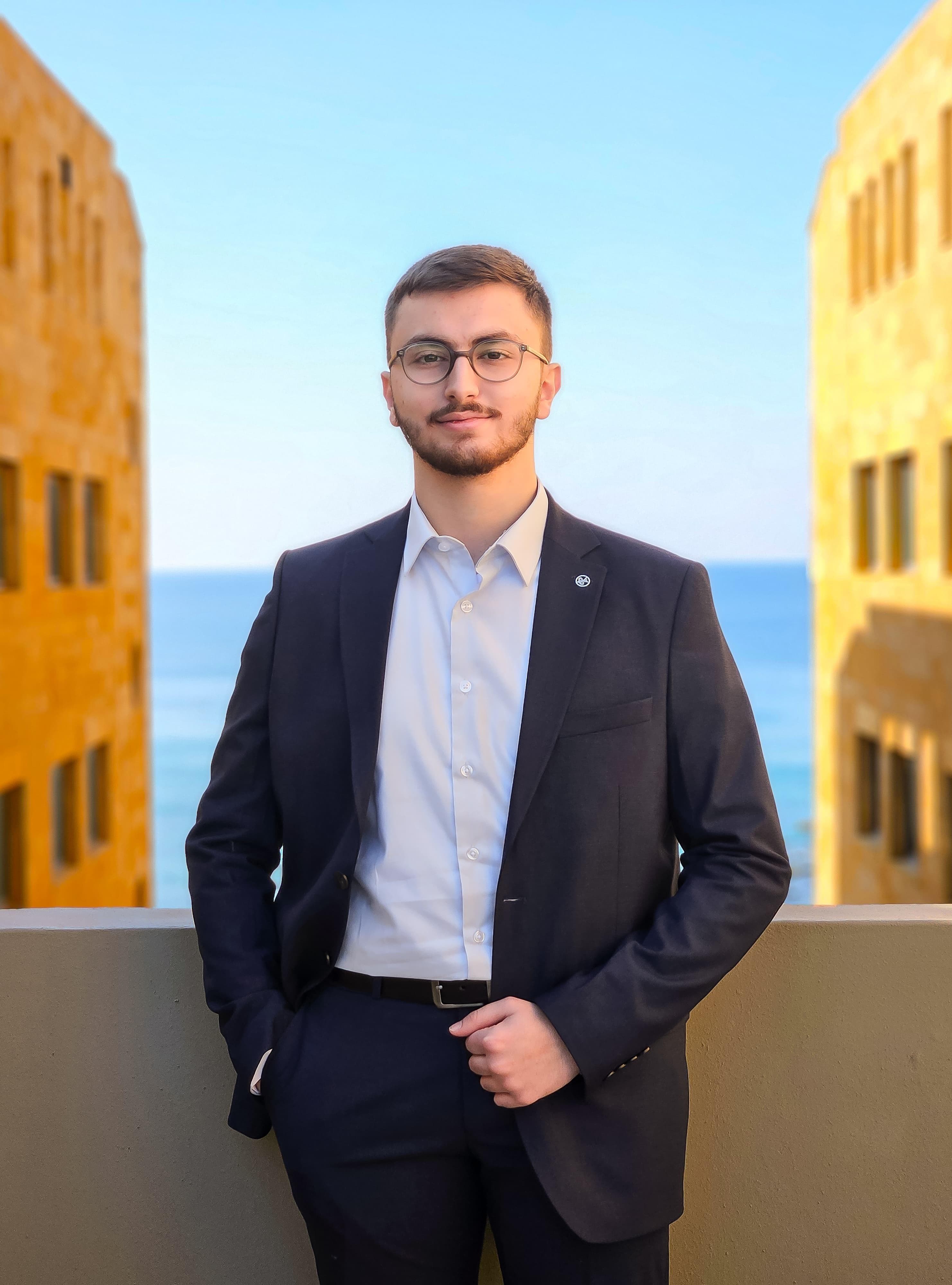 Bader Othman in a suit with the sea and stone buildings behind him